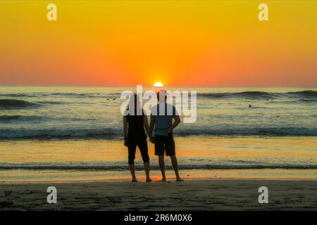 Couple hold hands on Guiones Beach where people gather to surf and watch at sunset, Playa Guiones, Nosara, Guanacaste, Costa Rica, Central America Stock Photo