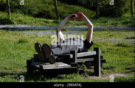 Kyiv, Ukraine May 5, 2023: A man lies on a bench looking at his phone Stock Photo