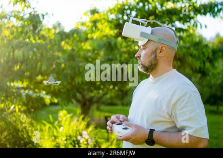 Male drone pilot operating tiny whoop FPV drone in the back yard. FPV experience with FPV glasses during sunset time. Technology and innovation concep Stock Photo