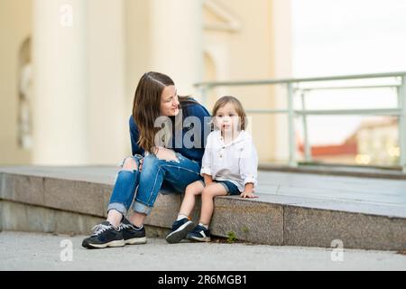 Cute funny toddler boy in his mothers arms. Mom and son having fun on sunny autumn day in a park. Adorable son being held by his mommy. Stock Photo