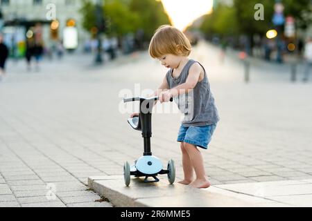 Funny toddler boy riding a baby scooter outdoors on summer day. Kid training balance on mini bike. Summer activities for small kids. Stock Photo