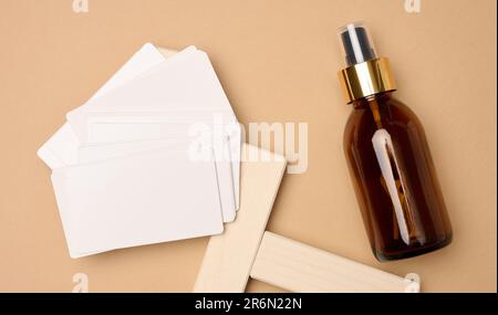 Glass brown bottle with cosmetic spray and paper business cards on brown background, top view Stock Photo