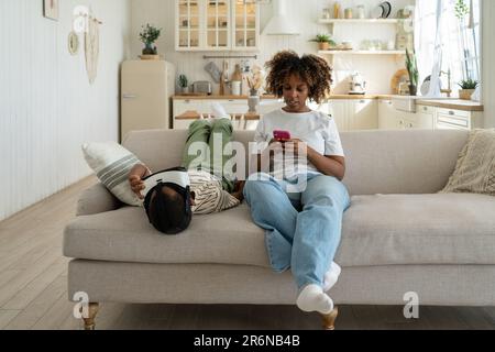 Mother and son relaxing home on sofa with digital devices. Mom us mobile phone, boy VR helmet  Stock Photo