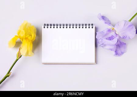 Notebook with clean page with purple and yellow flowers irises on orange background. Flat lay style. Stock Photo