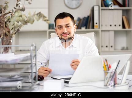 Positive man bookkeeper doing paperwork in office Stock Photo