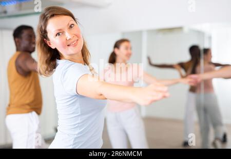 Excited young middle-aged men and women couples turning to sides during pair dance practicing in studio for adults Stock Photo