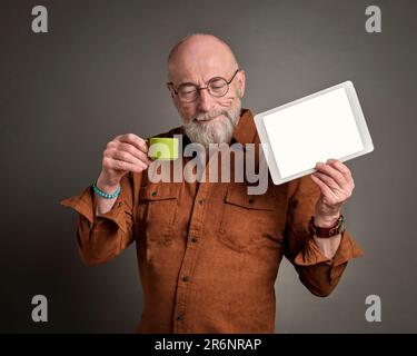 smiling senior man is drinking coffee and showing a blank digital tablet Stock Photo