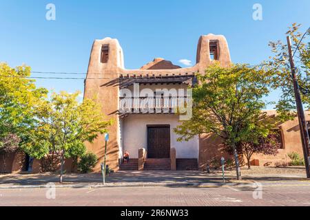Horizontal image of a man in an orange shirt sitting on the steps of the Pueblo-Revival style building that houses the New Mexico Museum of Art in San Stock Photo