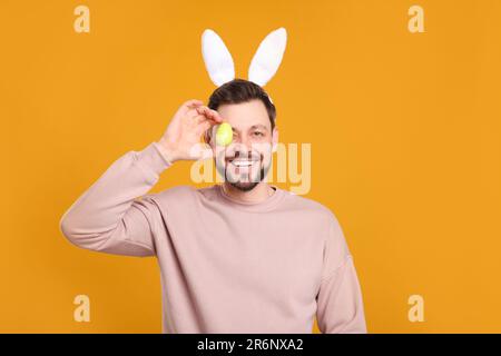 Happy man in bunny ears headband holding painted Easter eggs near his eyes  on orange background Stock Photo - Alamy