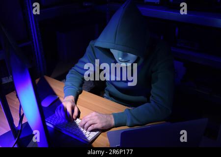 Hacker in mask working with computers in dark room. Cyber attack Stock Photo