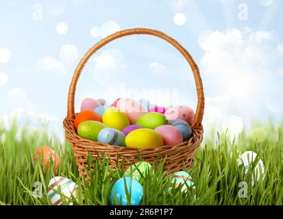 Wicker basket with festively decorated Easter eggs in green grass on sunny day Stock Photo