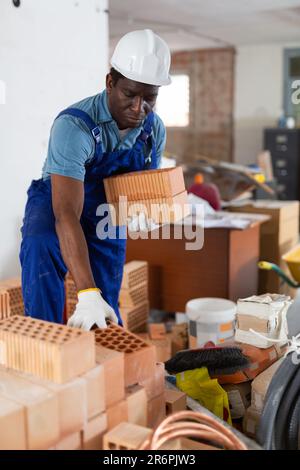 Builder in overall and hardhat carrying bricks in apartment Stock Photo