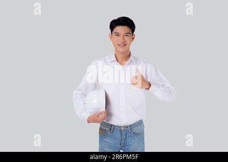 Portrait young asian man is engineer holding helmet smiling and thumbs up with confident isolated on white background, handsome male is architect or c Stock Photo