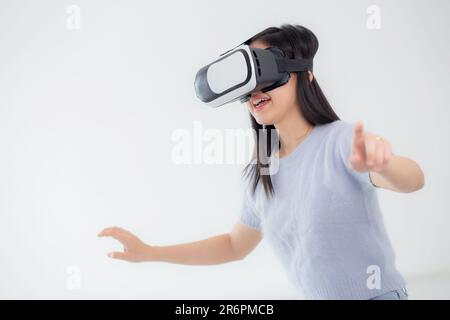 Young asian woman wearing vr headset playing game with excited in the bedroom at home, female using virtual reality or metaverse innovation for simula Stock Photo