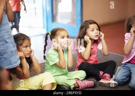 School children on floor listening to teacher for anatomy education, hearing exercise and learning in classroom. Class, group and kids on ground with Stock Photo