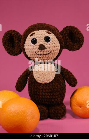 Children toy soft knitted brown Cheburashka on pink . DIY concept. Handmade work. Hobbies needlework sewing and knitting with woolen threads. Characte Stock Photo