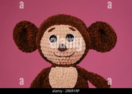 Children toy soft knitted brown Cheburashka on pink background. DIY concept. Handmade work. Hobbies needlework sewing and knitting with woolen threads Stock Photo