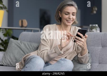 Cheerful pretty grey haired woman typing message Stock Photo