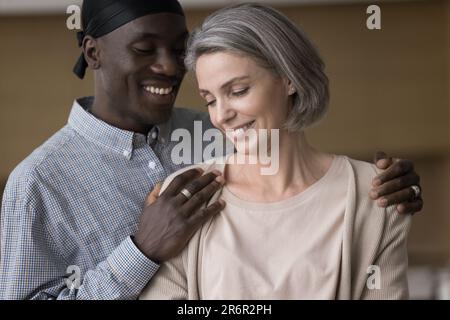 Happy handsome young African man hugging pretty grey haired girlfriend Stock Photo