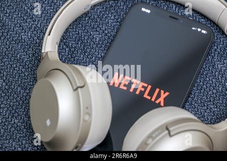 Netflix on smartphone, Netflix logo displayed on screen, gold headphones around device, online streaming concept, Netflix is popular global streaming Stock Photo