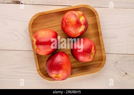 Several ripe nectarines with a wooden tray on a wooden table, macro, top view. Stock Photo