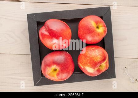 Several ripe nectarines with a wooden tray on a wooden table, macro, top view. Stock Photo