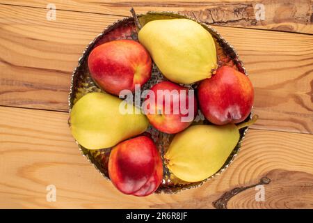 Several ripe nectarines and pear with metal vase on wooden table, macro, top view. Stock Photo