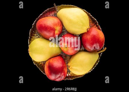 A few ripe nectarines and a pear with a metal vase on a black background, macro, top view. Stock Photo