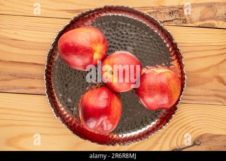 Several ripe nectarines with a metal tray on a wooden table, macro, top view. Stock Photo