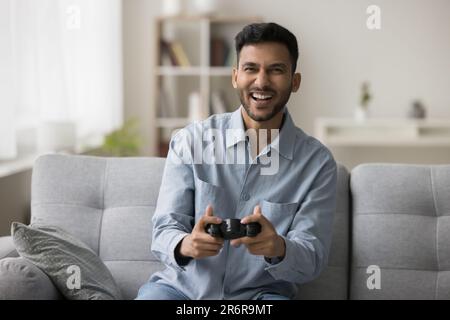 Joyful young Indian gamer guy playing videogame at home Stock Photo