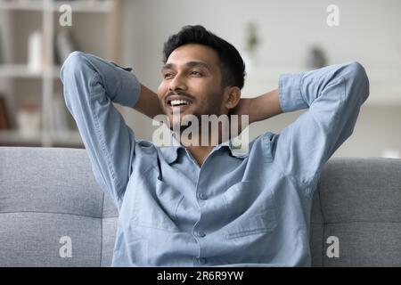 Cheerful young Indian man resting on couch, leaning on back Stock Photo