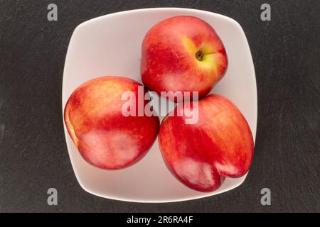 Three organic nectarines with a white plate on a black background, macro, top view. Stock Photo
