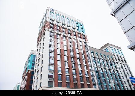 new brick building, red, white, grey, blue modern apartment building on white cloudy sky, residential complex. view from below from street. Stock Photo