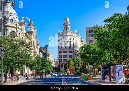 Valencia, Spain - July 15, 2022: A cityscape of buildings and trees with a sky background. Incidental people are visible on the street sidewalk. Stock Photo