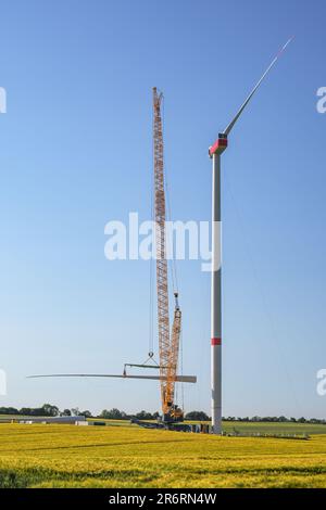 Giant construction site for a wind turbine, crane is lifting the second blade to install it onto the tower, heavy industry for renewable energy in a r Stock Photo