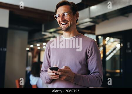 Male professional holding a mobile phone while standing in an office. Happy business man using a cellphone to send a text message in a modern workplac Stock Photo