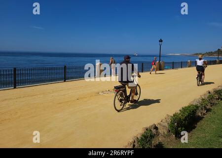 Couple riding bikes along promenade by the mediterranean sea, Marbella, Spain. Stock Photo
