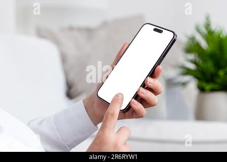 Woman holds modern smartphone, dressed in a white shirt, standing in living room. Isolated mobile screen for app or web page presentation Stock Photo