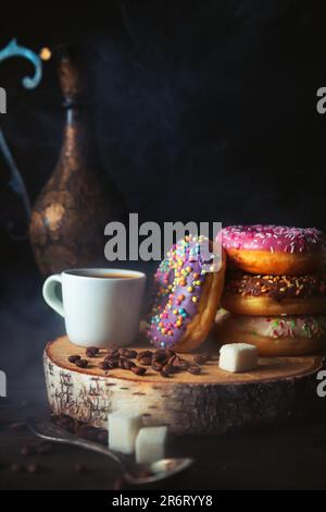 Stack of assorted donuts and a cup of steaming coffee on a dark background. Stock Photo