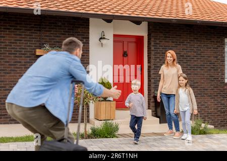 Father came home from the trip and happy son, daughter and wife running to meet him Stock Photo