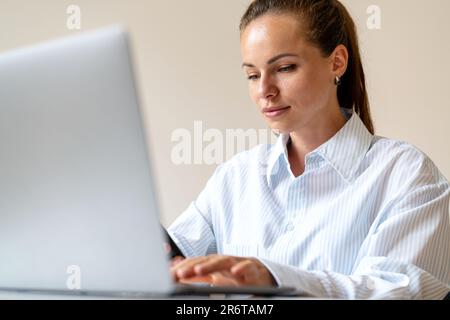 Young brunette woman working on her laptop, businesswoman working in the office sitting at the desk and using computer. Stock Photo