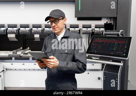 Worker with digital tablet controls automatic machine tool in smart factory Stock Photo