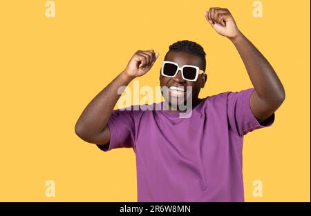 Happy African Man Wearing Sunglasses Shaking Fists Over Yellow Background Stock Photo