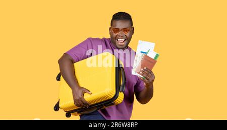 Black Man With Suitcase Showing Tickets Wearing Sunglasses, Yellow Background Stock Photo