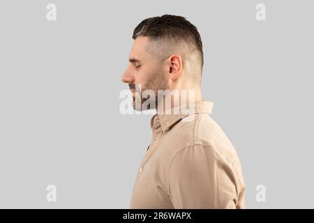 Profile shot of middle aged bearded man in shirt standing with closed eyes over light background, side view, copy space Stock Photo