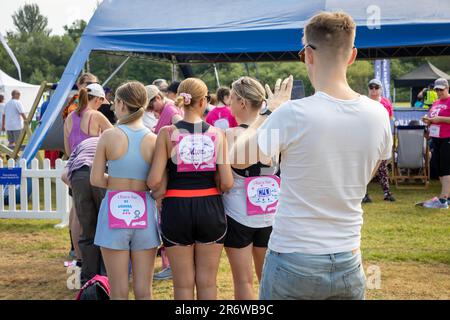 Warrington, Cheshire, UK. Sunday 11 June 2023; Warrington, Cheshire, UK; Race for Life in Victoria Park in aid of Cancer Research. Hundreds of people dressed in pink and competed in different fundraising events in aid of Cancer Research. A male takes a photo of three girls who have a message on their backs. Credit: John Hopkins/Alamy Live News Stock Photo