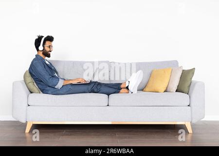 Cheerful arab man developer working from home, using laptop, headphones Stock Photo