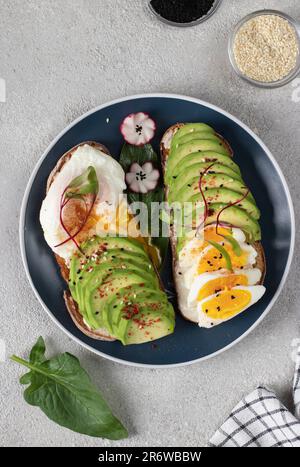 Healthy breakfast - sandwiches with avocado, egg and sesame on round plate on gray table, Top view Stock Photo