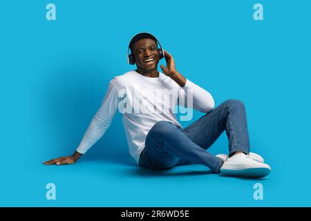 Joyful handsome young african guy listening to music on blue Stock Photo