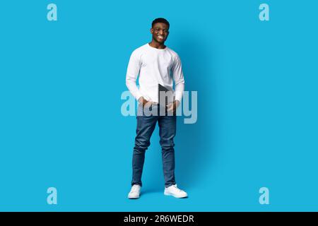 Cool black guy software engineer posing with laptop, blue background Stock Photo